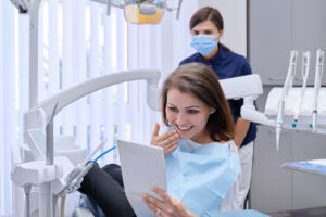 middle aged woman with doctor dentist looking in mirror at teeth, sitting in dental chair