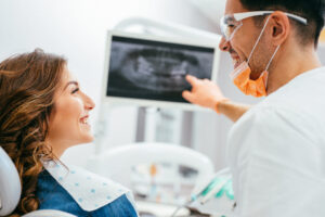 Smiling woman in a dentist's chair reviewing an X-ray of missing teeth, discussing dental bridge options.